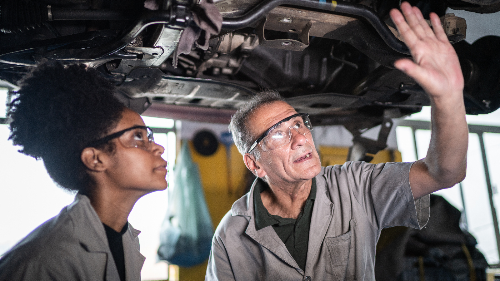 A shop owner trains a new technician at a shop.