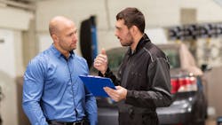 A shop manager talks to an auto technician. A shop manager talks to an auto technician.
