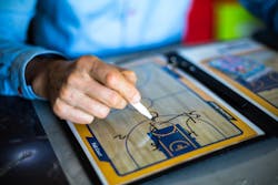 A basketball coach draws up a play on his board. A basketball coach draws up a play on his board.