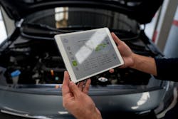 An automotive technician uses a tablet to get repair information to work on a car. An automotive technician uses a tablet to get repair information to work on a car.