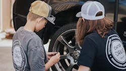 A youth looks over a car with a technician.