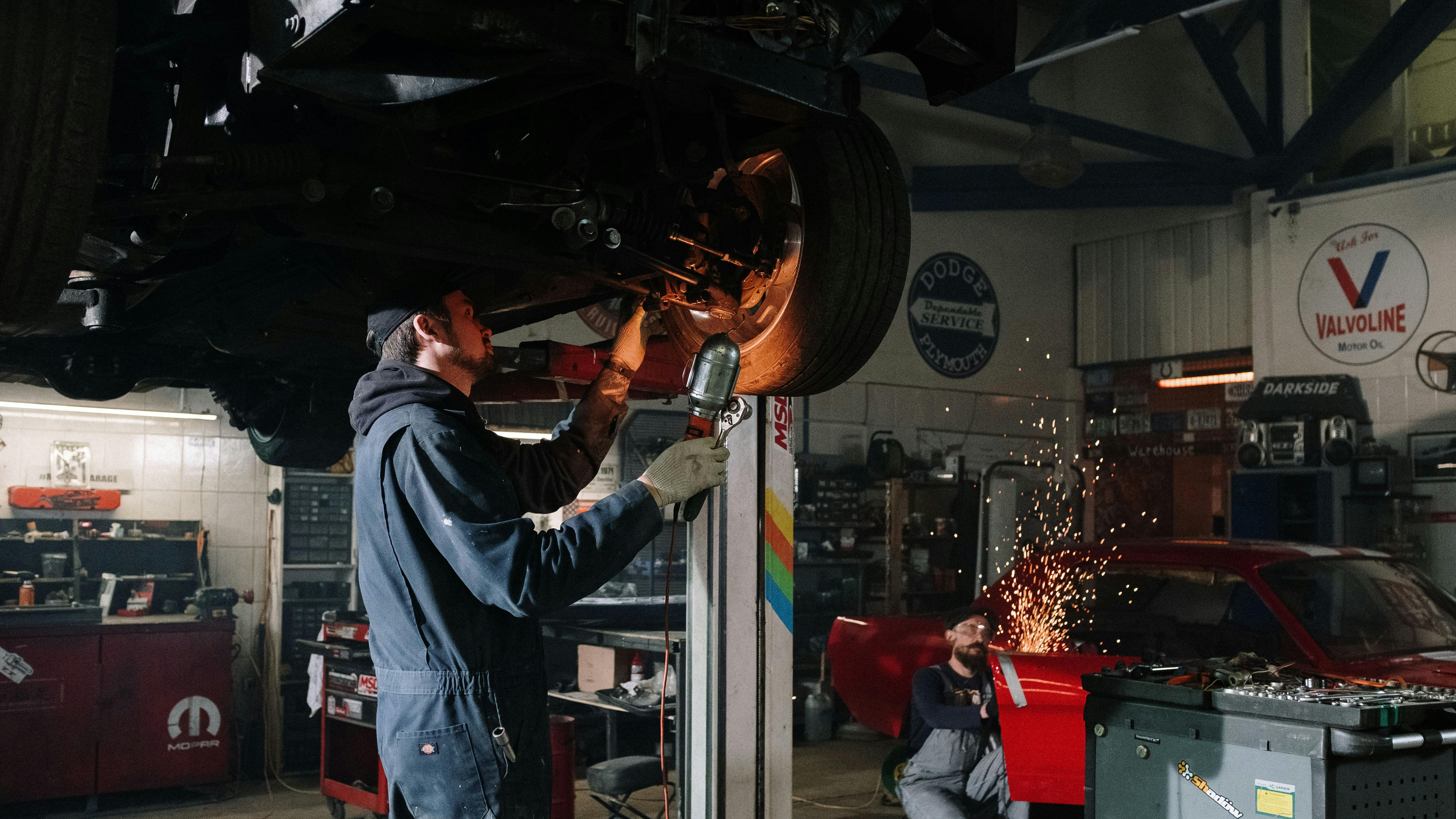 a mechanic examines a car on a lift while another mechanic saws metal