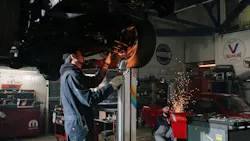 a mechanic examines a car on a lift while another mechanic saws metal